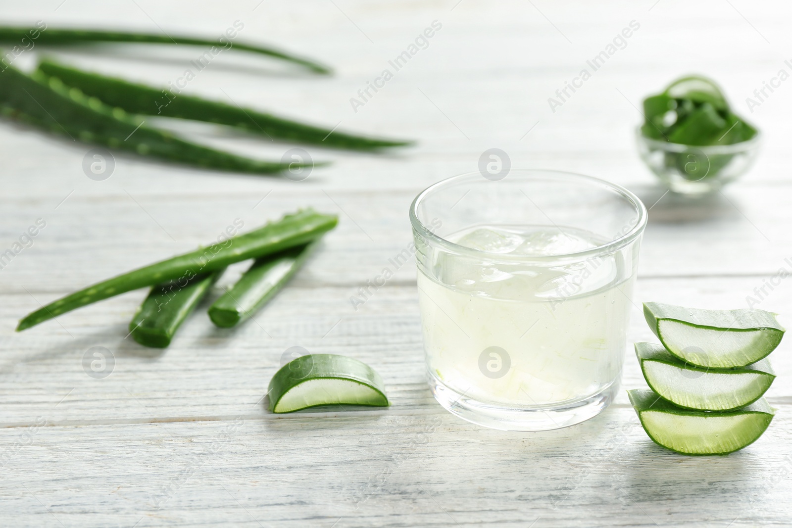 Photo of Glass with aloe vera gel and green leaves on wooden table. Space for text