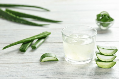 Photo of Glass with aloe vera gel and green leaves on wooden table. Space for text