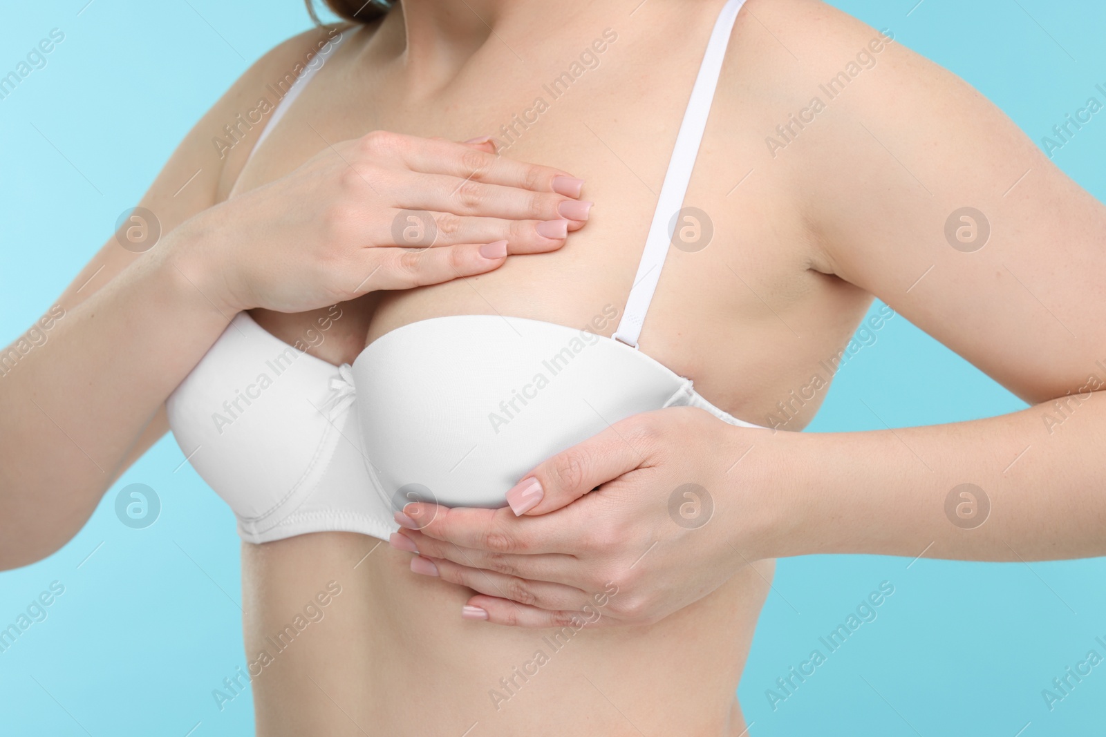 Photo of Mammology. Young woman doing breast self-examination on light blue background, closeup