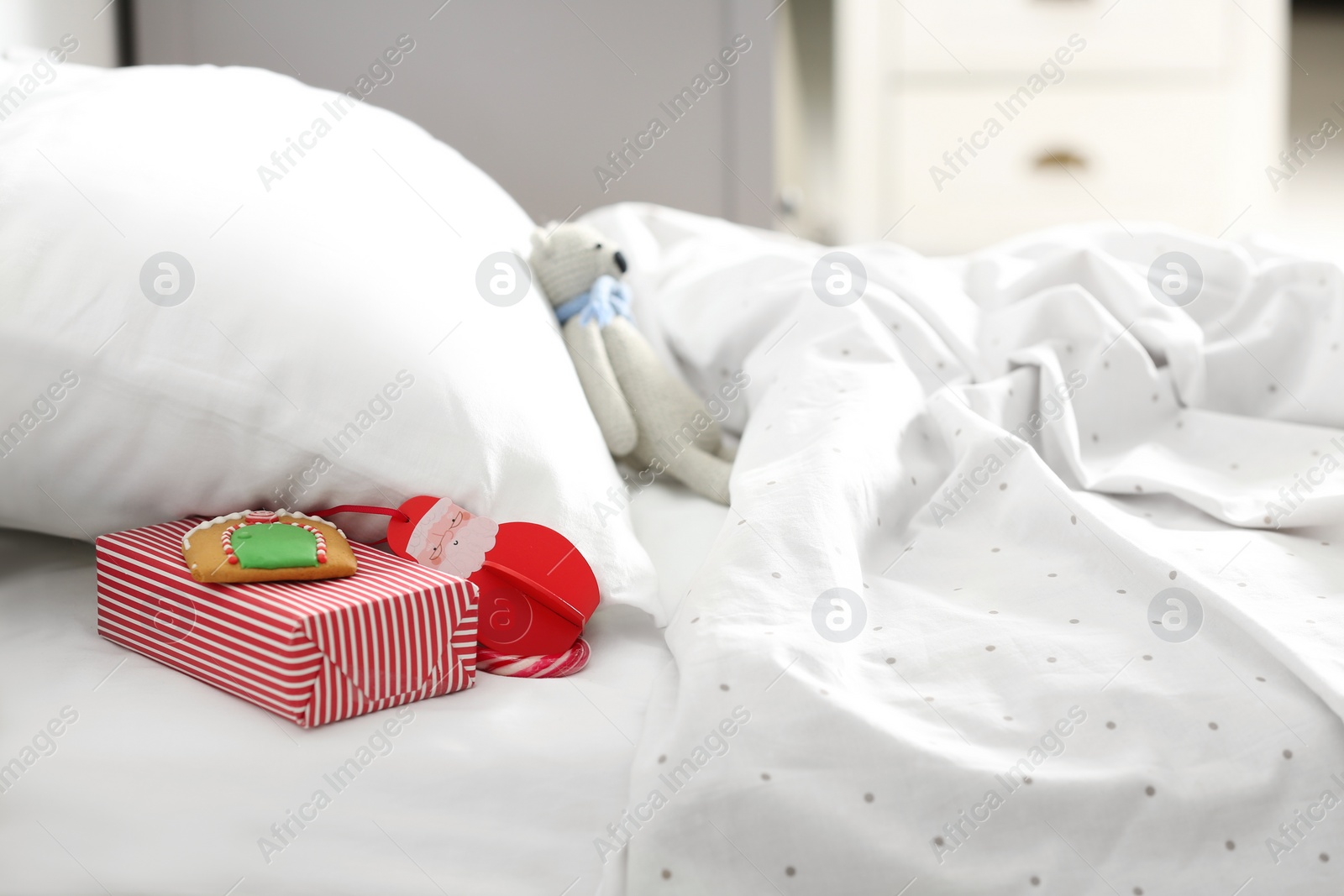 Photo of Gift box with candy cane and gingerbread under pillow in children's bedroom. St. Nicholas Day tradition