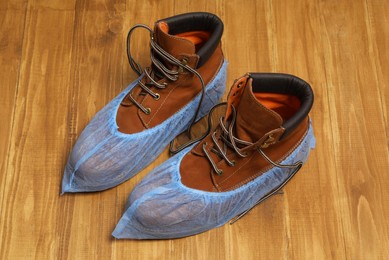 Photo of Men`s boots in blue shoe covers on wooden floor