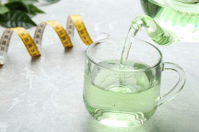 Pouring herbal diet tea into cup at light table with measuring tape