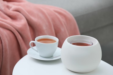 Photo of Wax air freshener and cup of hot tea on white table indoors. Interior element