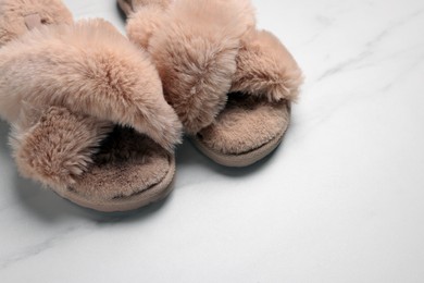 Pair of soft slippers on white marble floor, closeup. Space for text