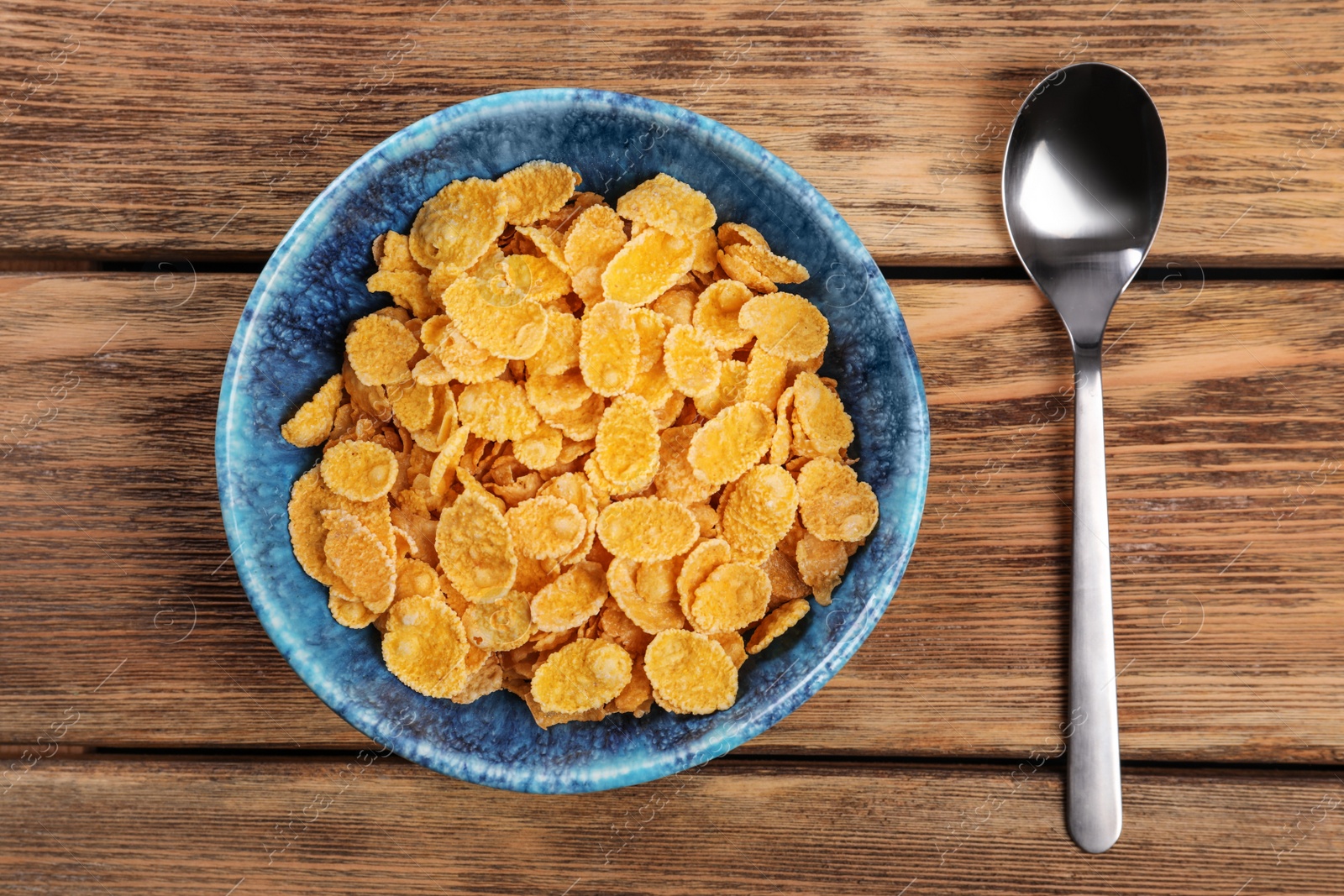 Photo of Bowl with healthy cornflakes and spoon on wooden table, top view