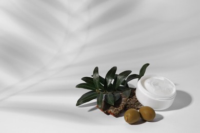 Photo of Jar of natural cream, stones and olives on white background, space for text. Cosmetic products