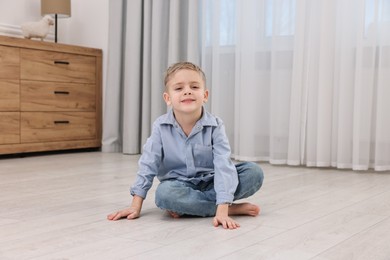 Photo of Cute little boy sitting on warm floor at home. Heating system