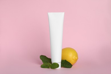 Photo of Blank tube of toothpaste, fresh mint and lemon on pink background