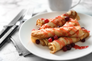 Photo of Thin pancakes with berries and syrup on plate, closeup