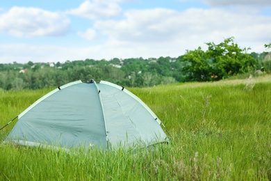 Photo of Modern camping tent in green field on sunny day. Space for text