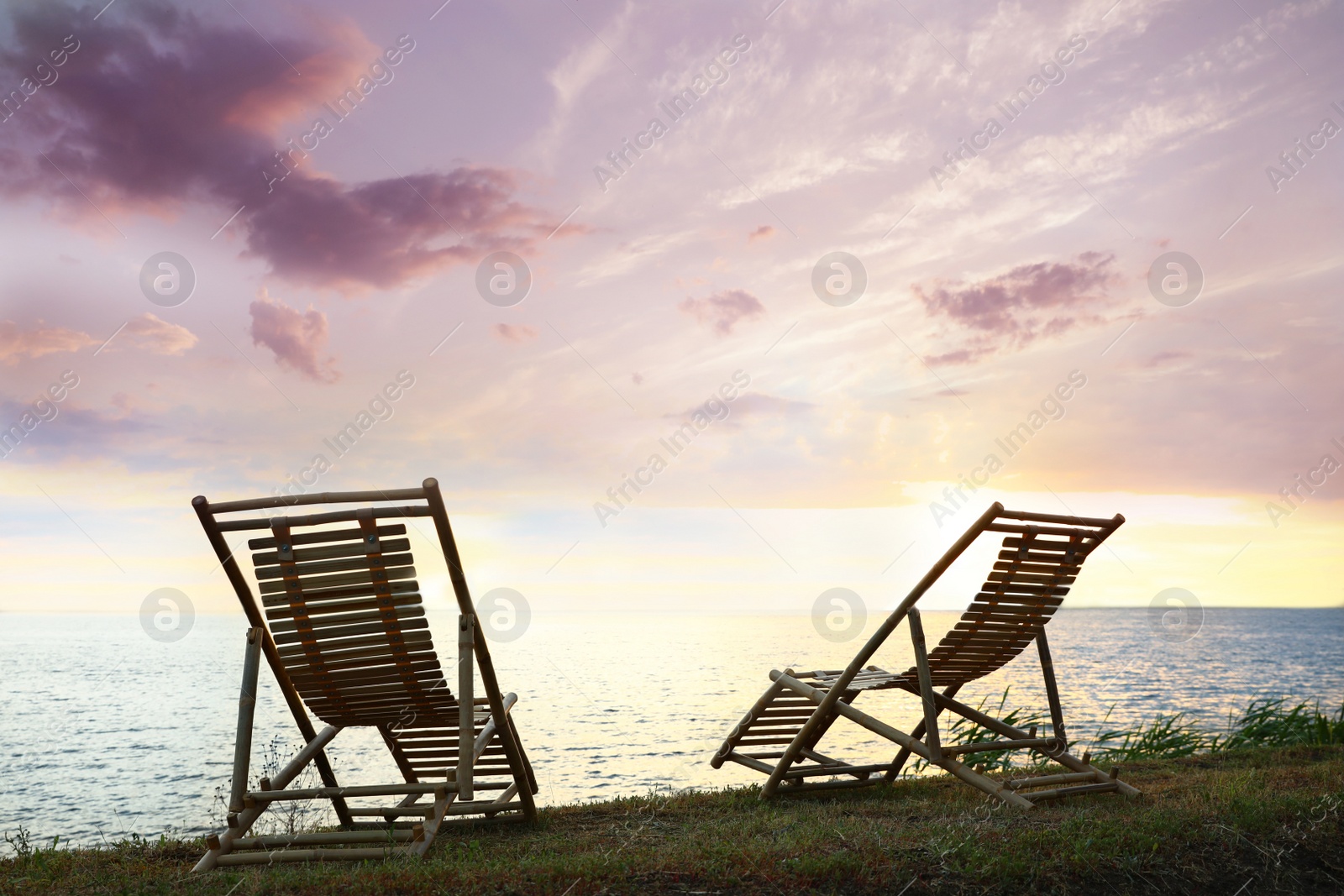 Photo of Empty wooden deckchairs on hill near calm river