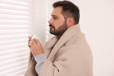 Photo of Sick man wrapped in blanket with tissue indoors. Cold symptoms