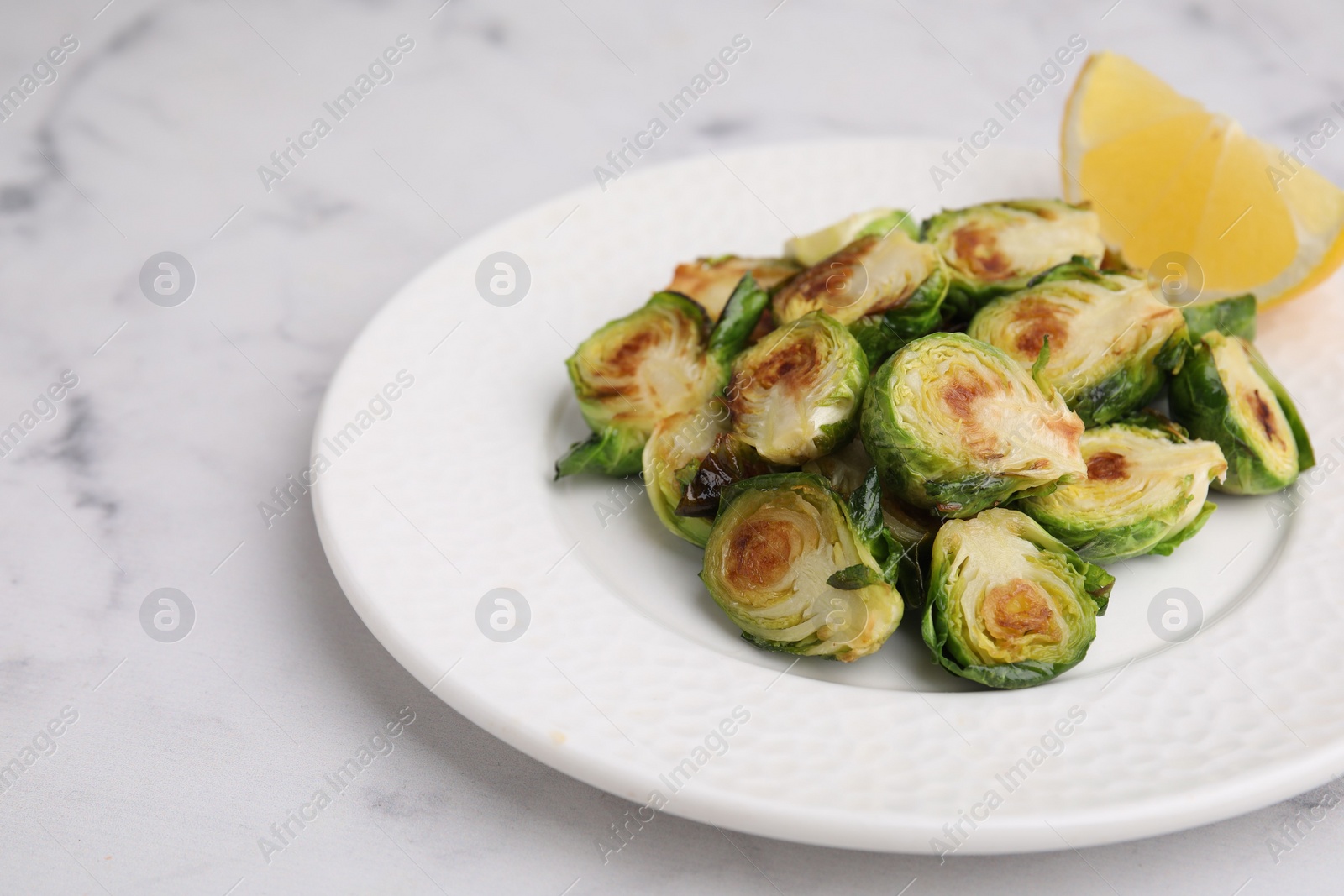 Photo of Delicious roasted Brussels sprouts and slice of lemon on white marble table, closeup