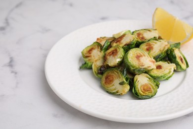 Delicious roasted Brussels sprouts and slice of lemon on white marble table, closeup