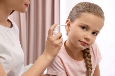 Mother spraying medication into daughter's ear at home