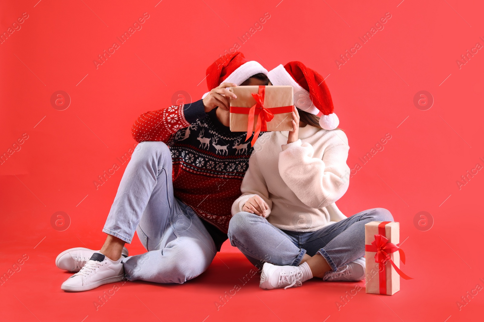 Photo of Couple covering their faces with Christmas gift on red background