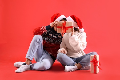 Photo of Couple covering their faces with Christmas gift on red background