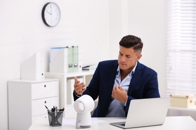 Man suffering from heat in front of fan at workplace