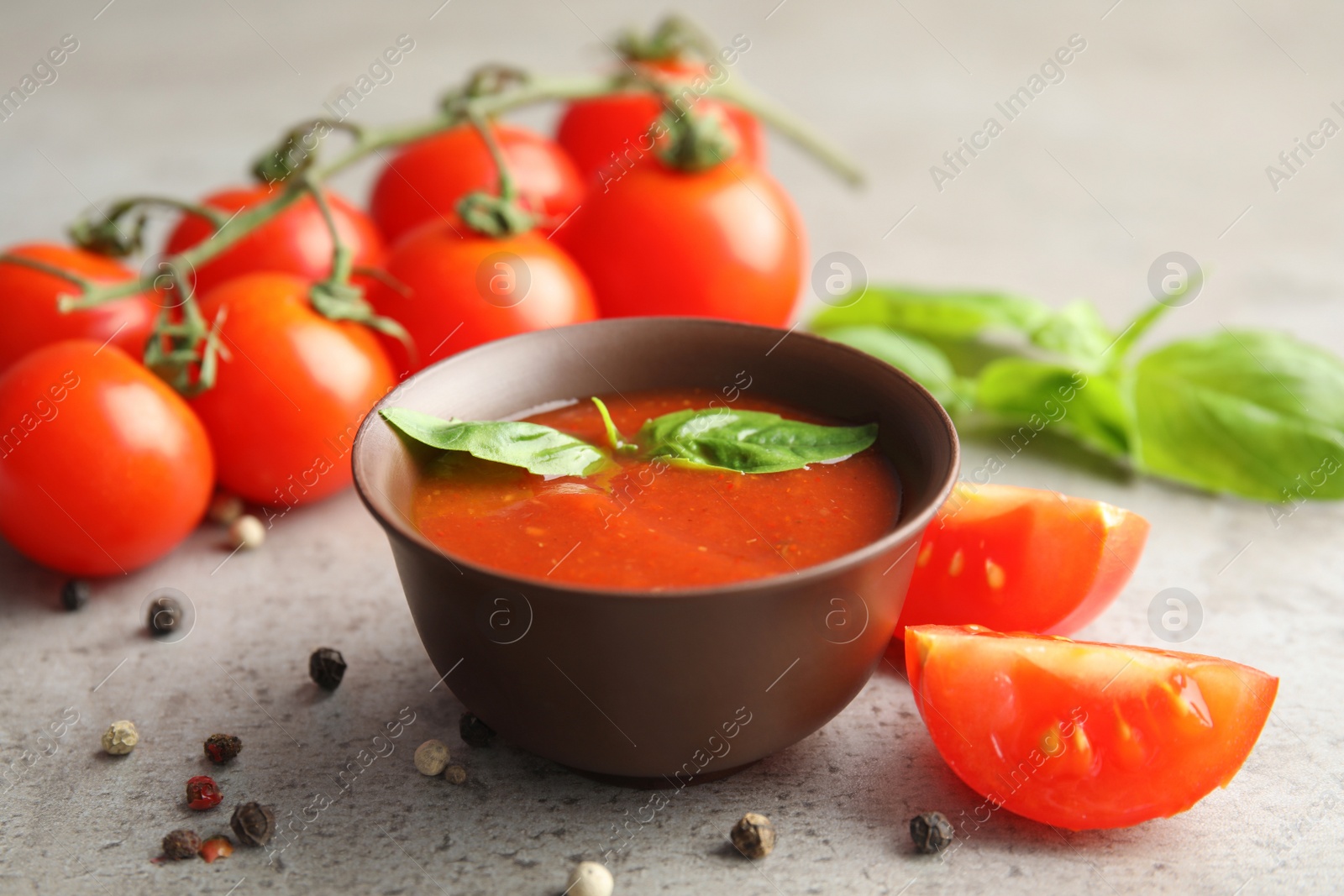 Photo of Bowl of sauce with basil and tomatoes on grey table