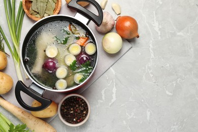 Photo of Pot with tasty bouillon and different ingredients on light grey table, flat lay. Space for text