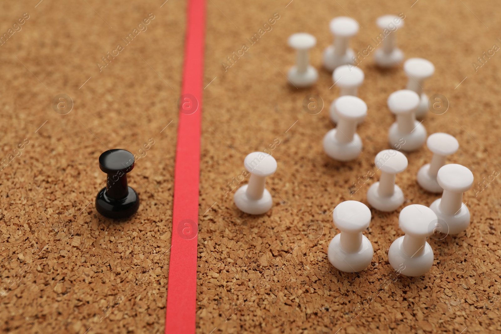 Photo of Black push pin separated from white ones by red strip in cork board, closeup. Racism concept