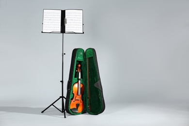 Photo of Violin in case and note stand with music sheets on grey background. Space for text