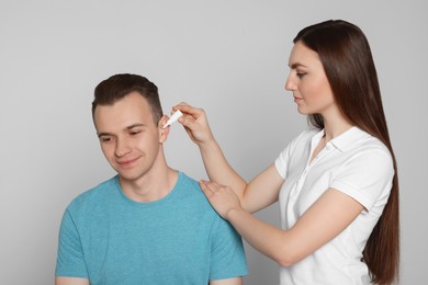 Woman dripping medication into man's ear on light grey background