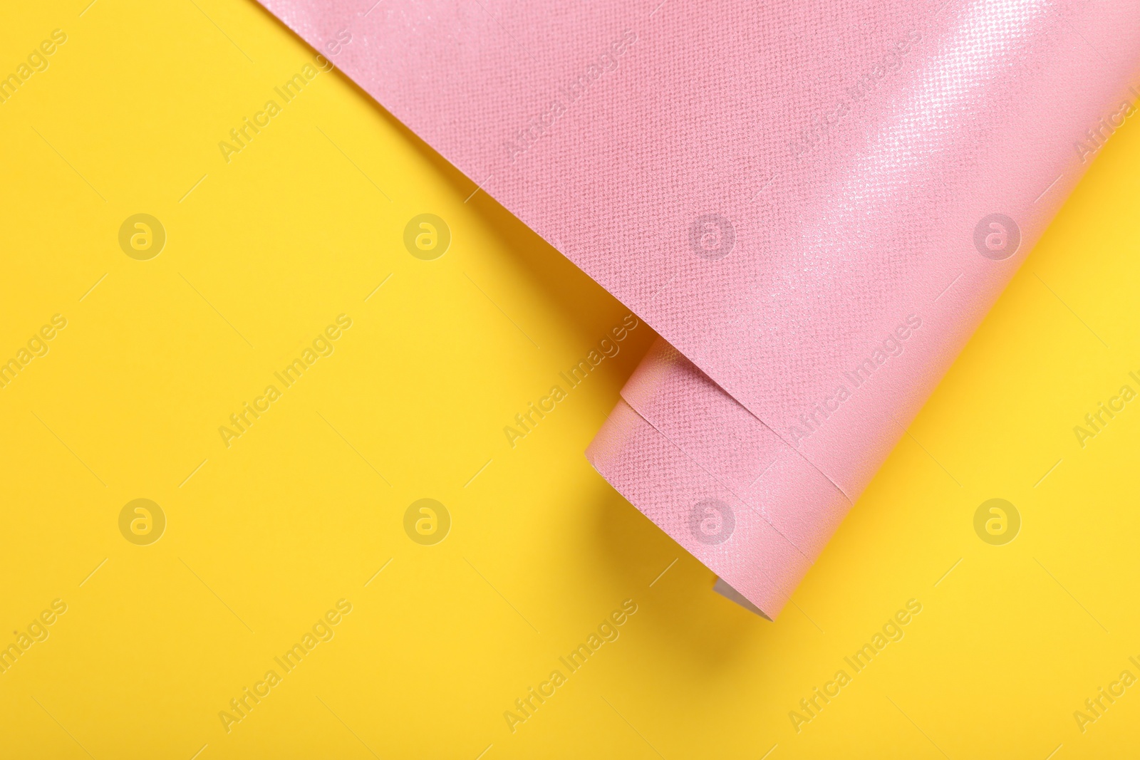 Photo of Roll of pink wrapping paper on yellow background, top view. Space for text