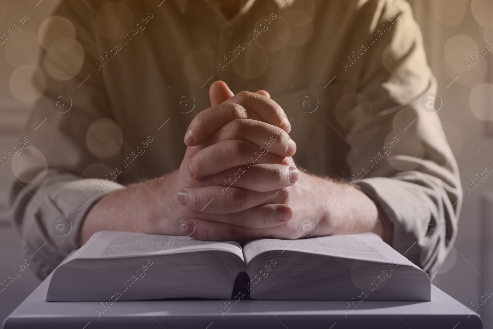 Image of Religion. Christian man praying over Bible at table, closeup. Bokeh effect