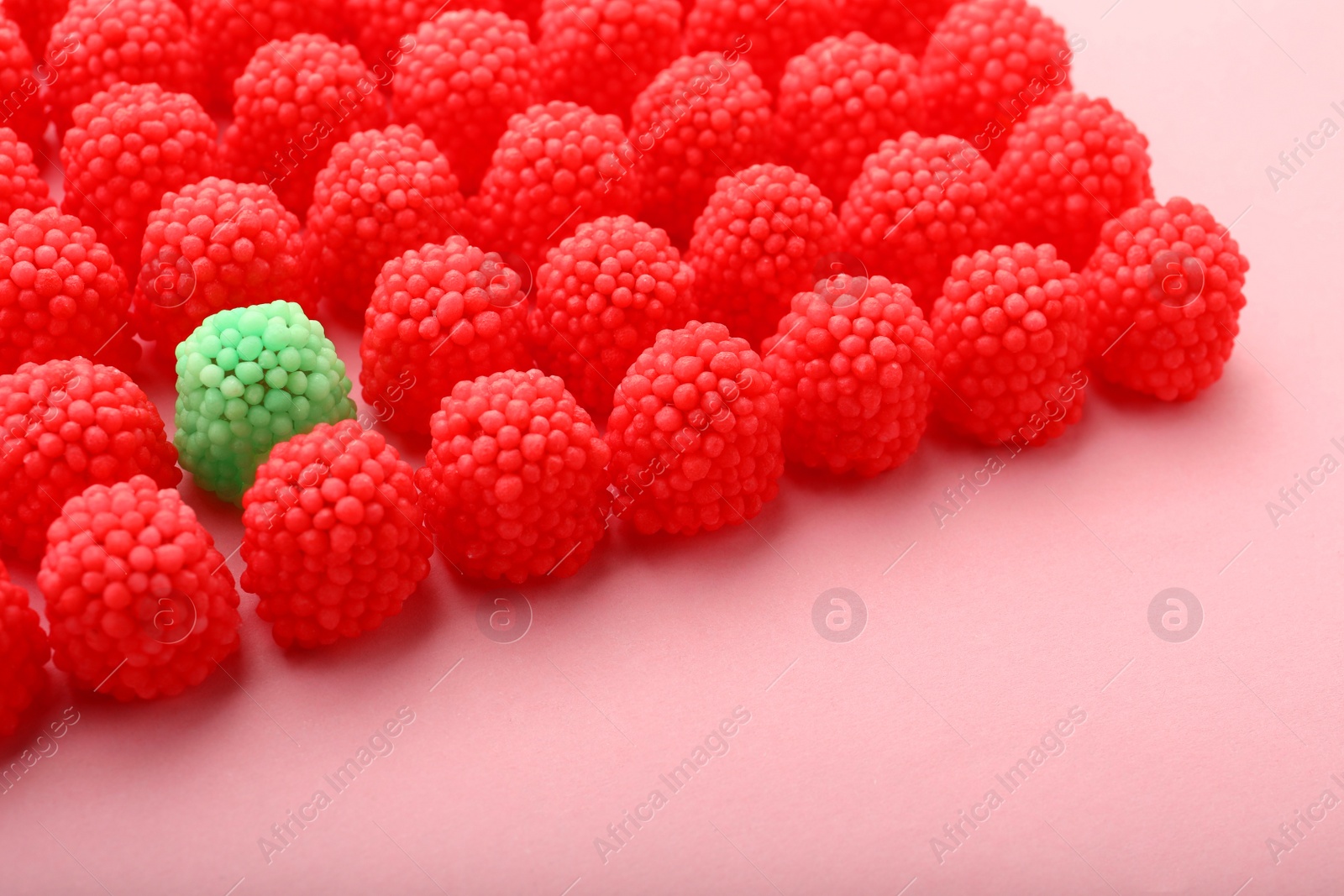 Photo of Delicious green gummy raspberry candy among red ones on pink background