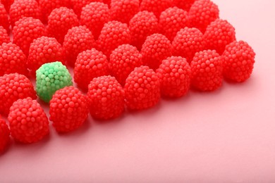 Photo of Delicious green gummy raspberry candy among red ones on pink background