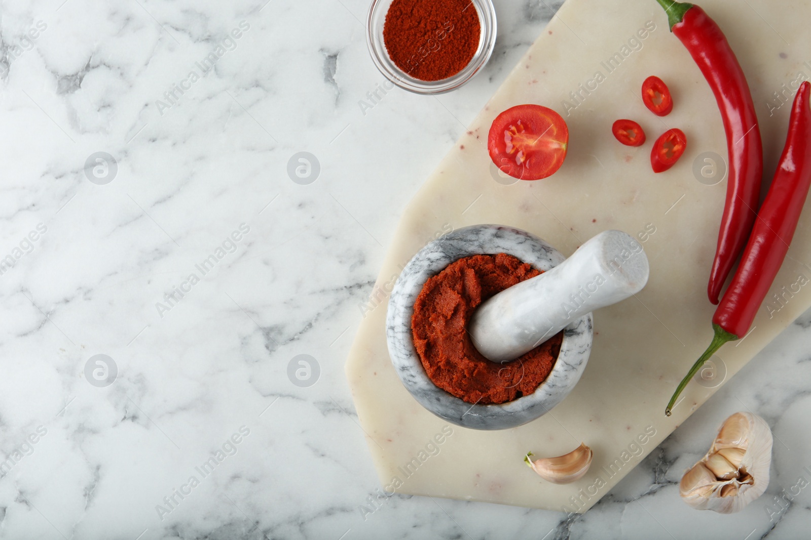 Photo of Red curry paste in mortar and ingredients on white marble table, flat lay. Space for text