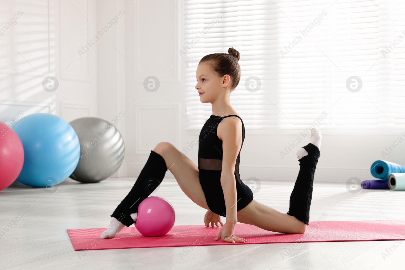 Photo of Cute little girl with ball doing gymnastic exercise indoors