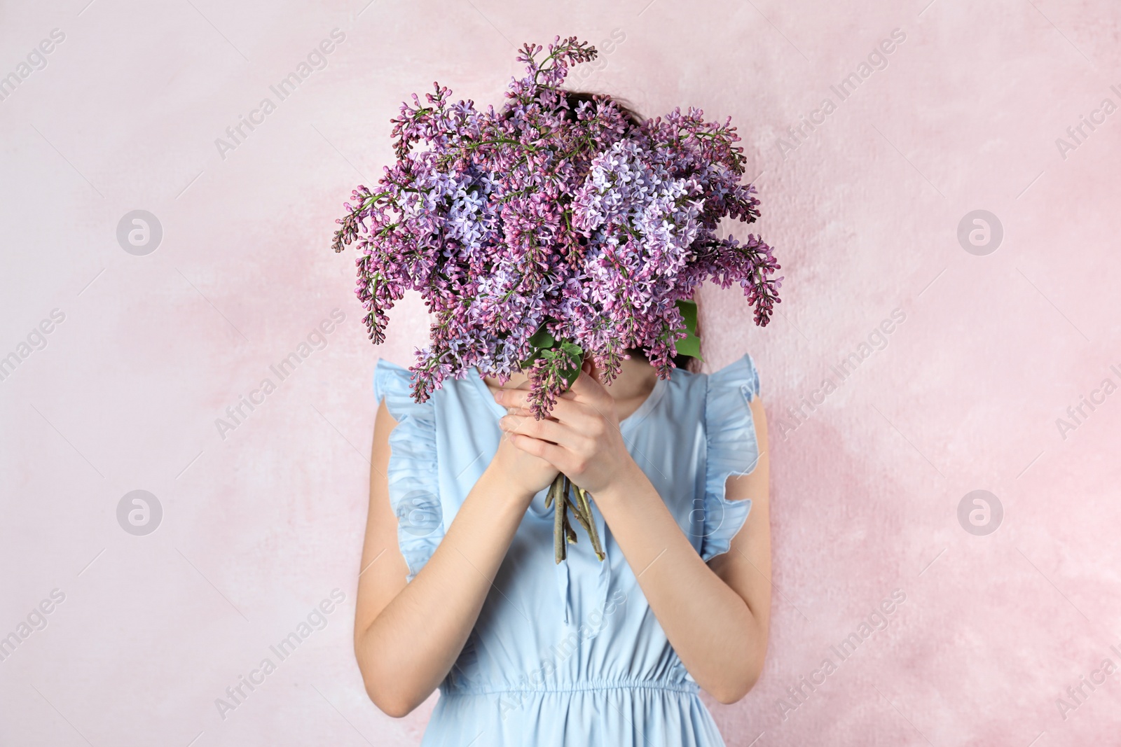 Photo of Woman closing face with bouquet of beautiful lilac flowers on color background