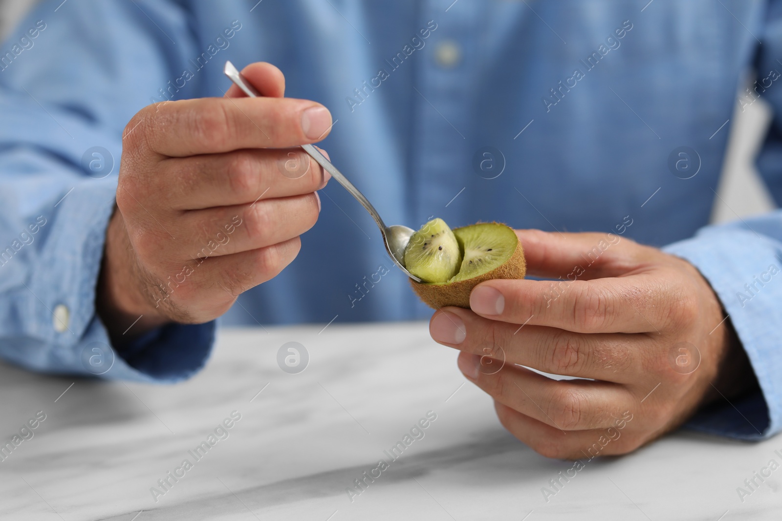 Photo of Man eating kiwi with spoon at white table, closeup