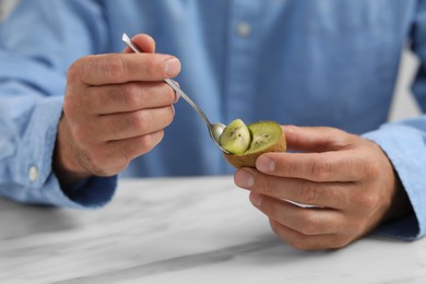 Man eating kiwi with spoon at white table, closeup
