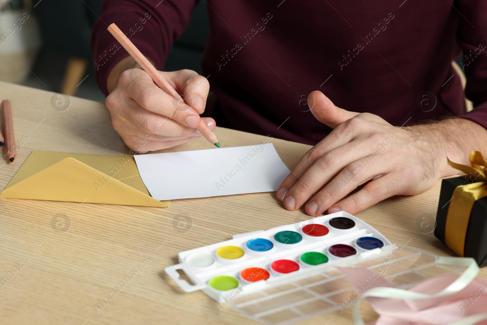 Photo of Man writing message in greeting card at wooden table, closeup