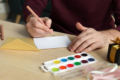 Man writing message in greeting card at wooden table, closeup