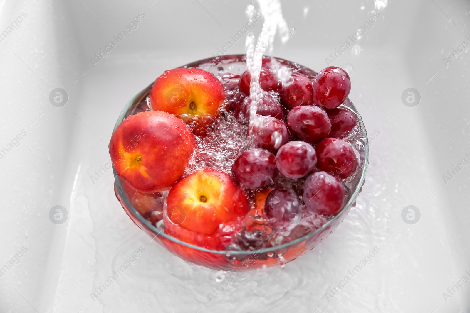 Photo of Washing fresh grapes and nectarines in bowl under tap water