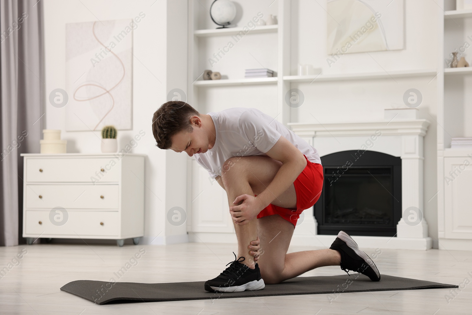 Photo of Man suffering from leg pain on mat at home