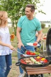 Photo of Young people having barbecue with modern grill outdoors