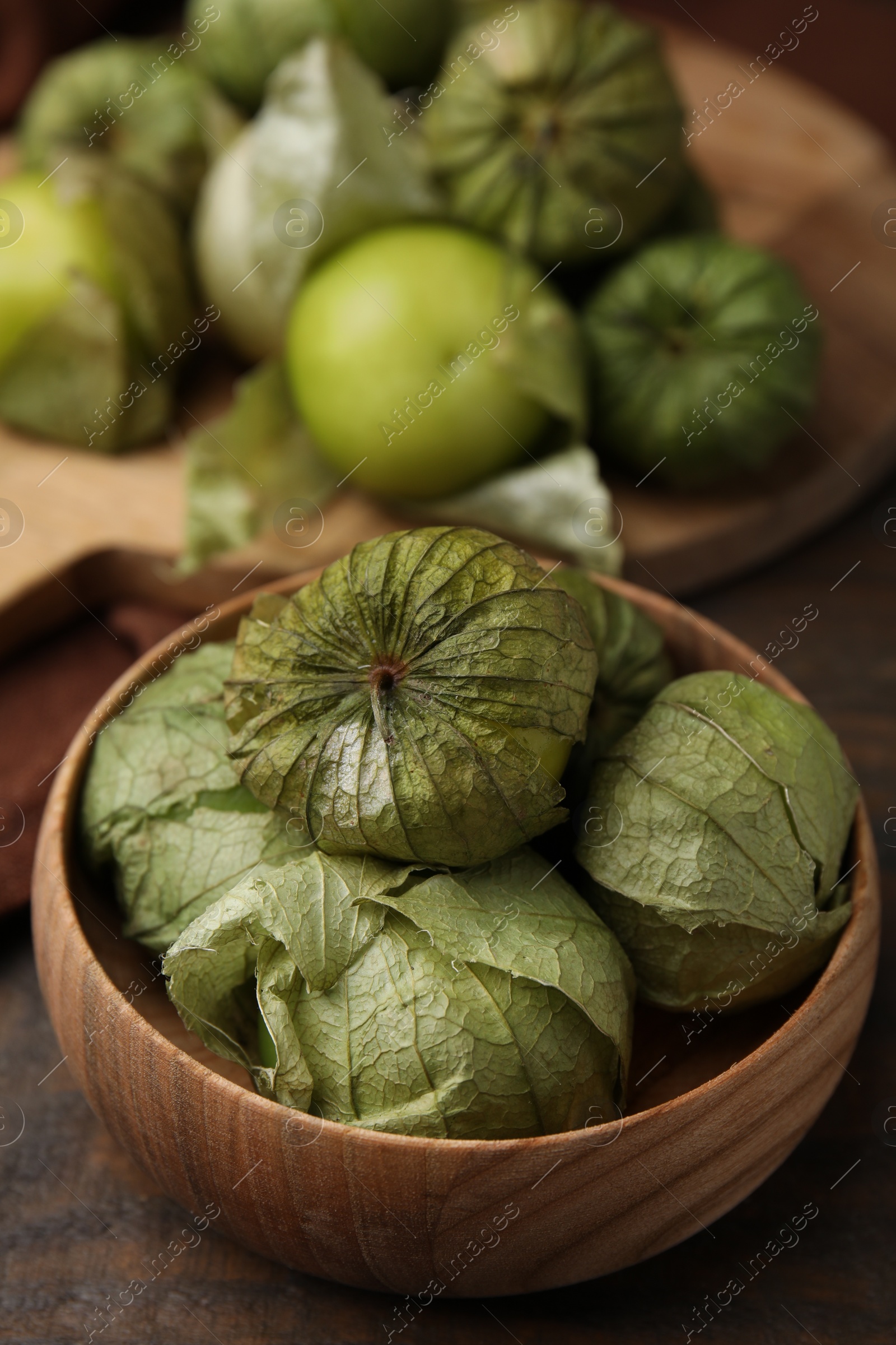 Photo of Fresh green tomatillos with husk in bowl on wooden table, closeup