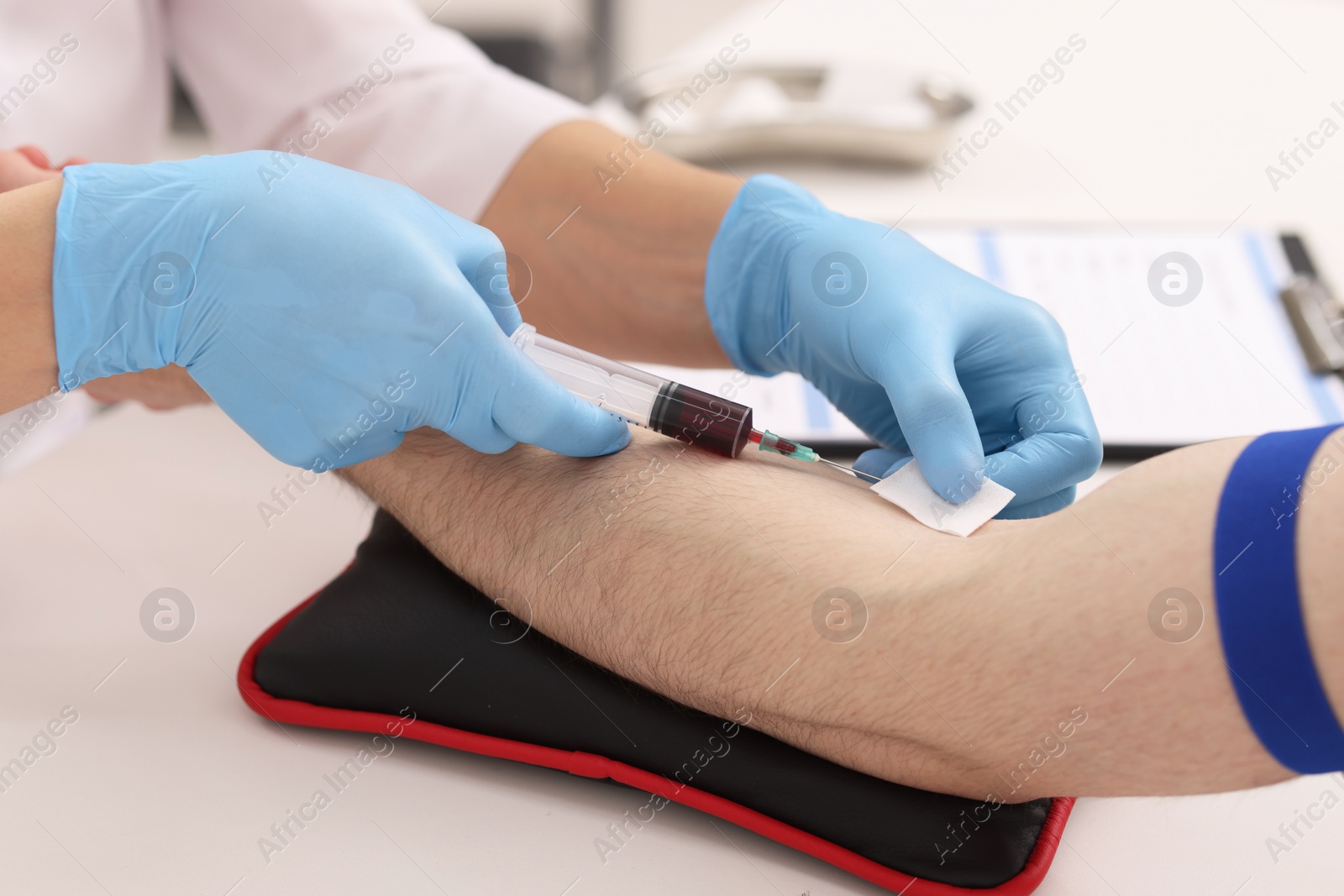 Photo of Doctor taking blood sample from patient with syringe at white table in hospital, closeup
