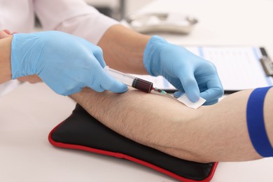 Doctor taking blood sample from patient with syringe at white table in hospital, closeup