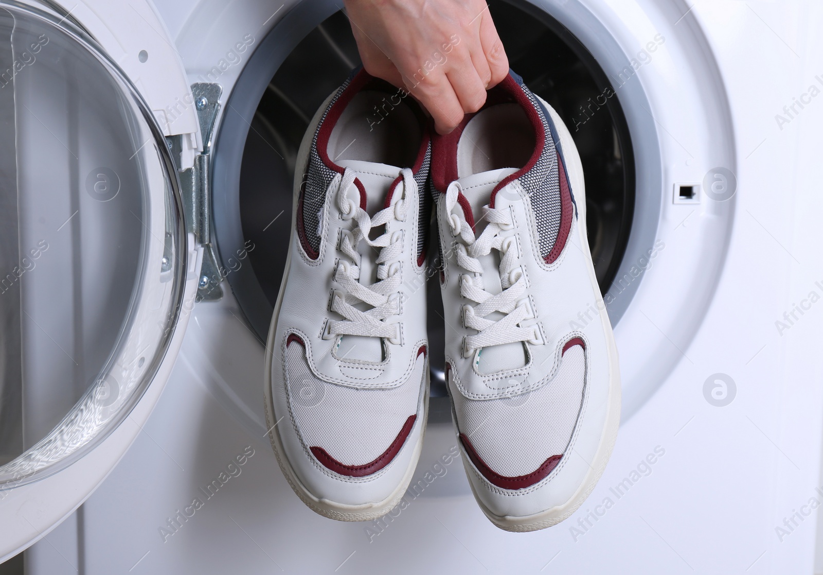 Photo of Woman putting pair of sport shoes into washing machine, closeup