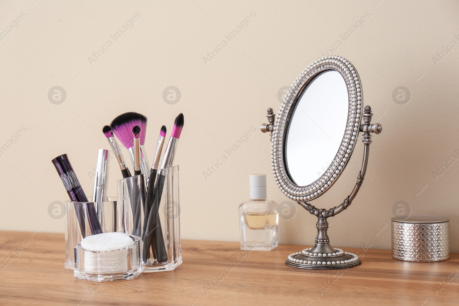 Photo of Organizer with cosmetic products for makeup and mirror on table against light wall