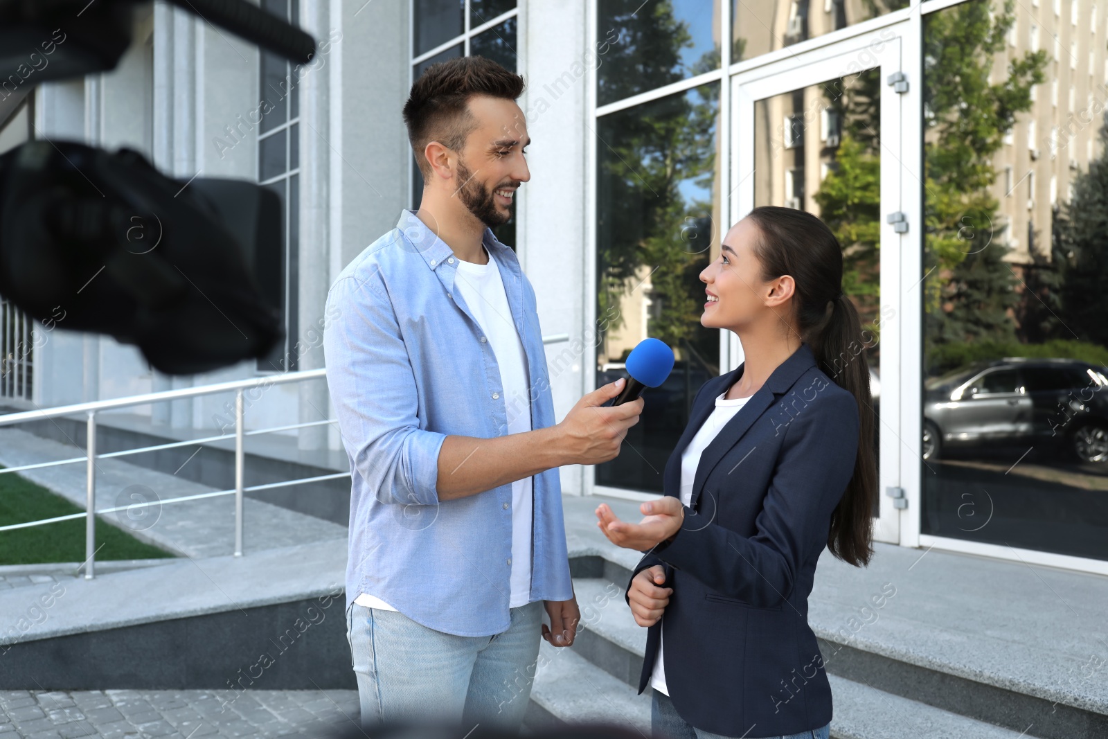 Photo of Professional journalist taking interview in front of video camera outdoors