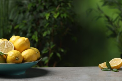 Fresh lemons and green leaves on grey table outdoors. Space for text