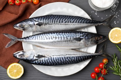 Raw mackerel, tomatoes and lemons on black wooden table, flat lay
