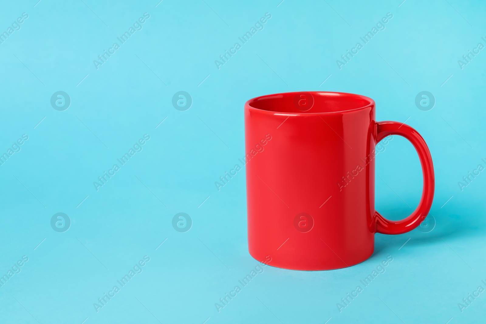 Photo of One red ceramic mug on light blue background, space for text